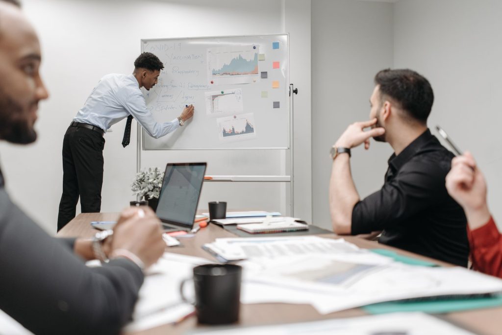 Two colleagues discussing a product roadmap on a screen, transitioning focus from technical details to market planning.